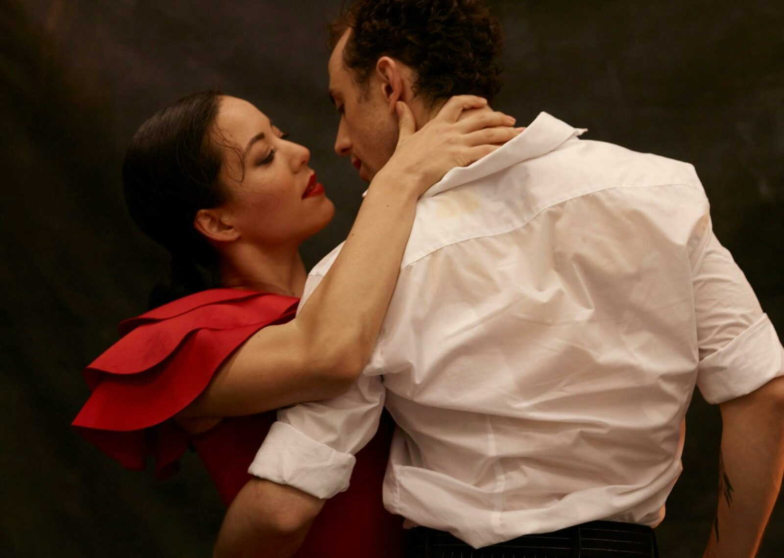 Dancer in a red dress passionately embracing a dancer in a white shirt
