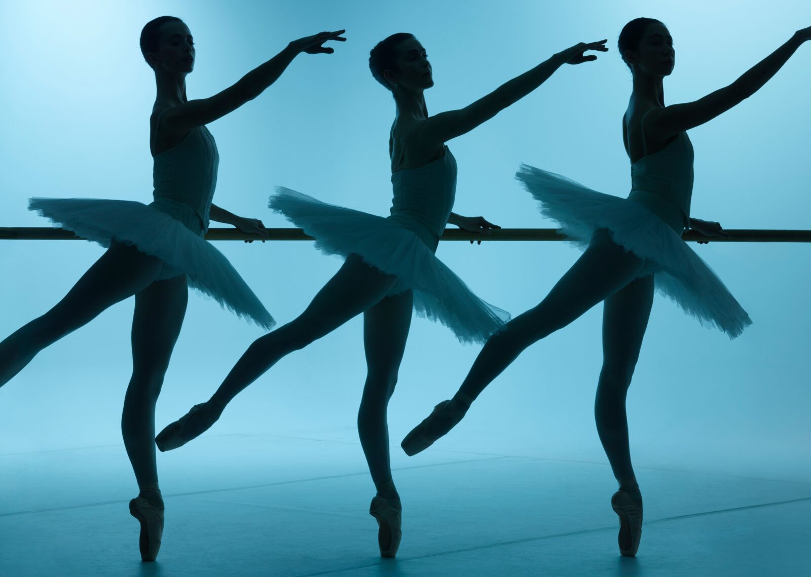 Three dancers standing in formation at the barre, with a blue background