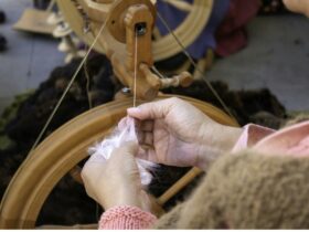 the hands of a spinner spinning wool into yarn with a spinning wheel