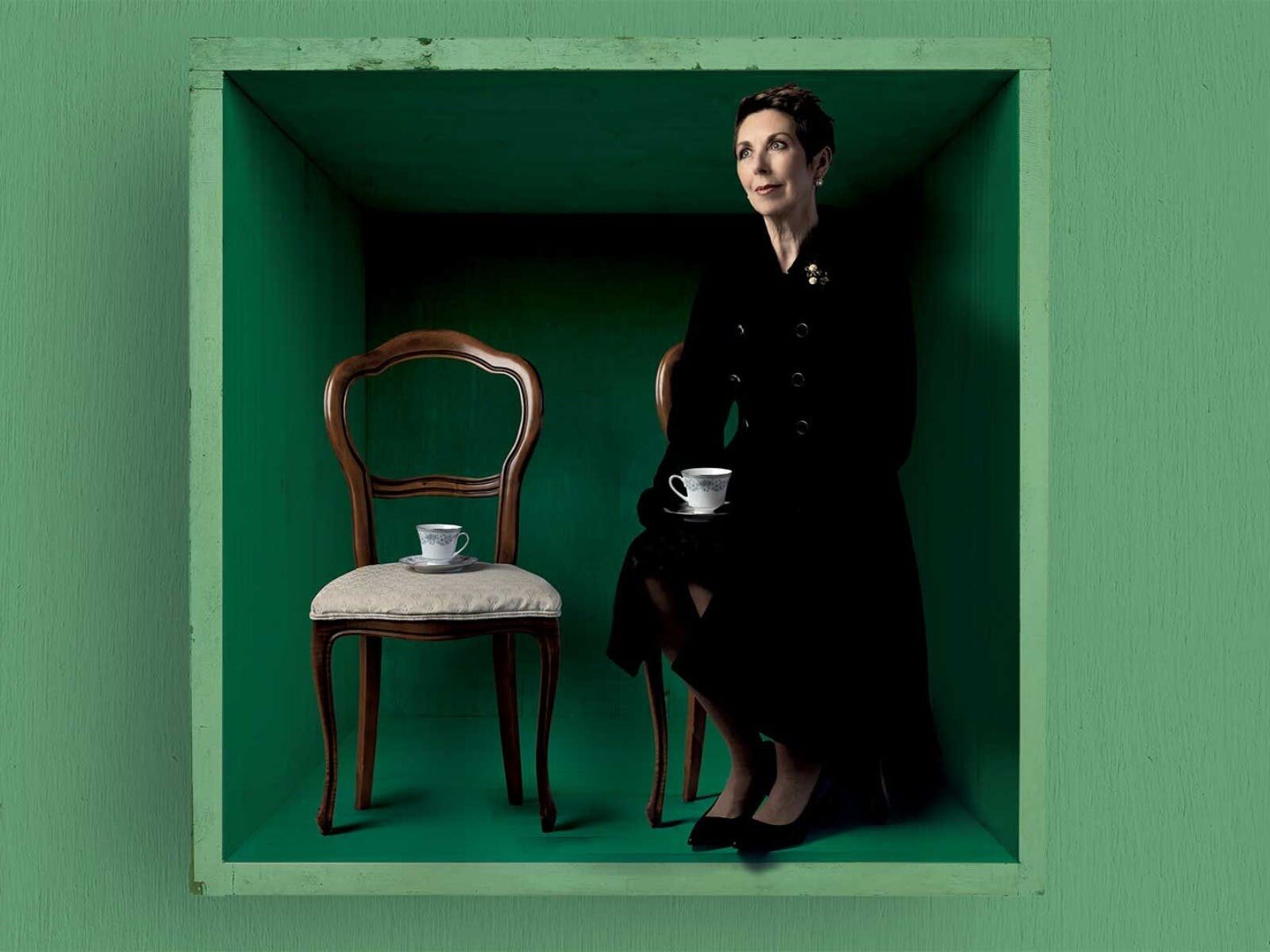 A woman sitting in a green box, savouring a cup of tea.