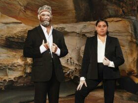Image of two First Nations Australians wearing suits and standing in front of a large rock
