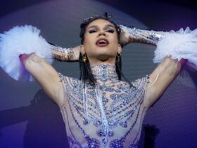 A performer wearing a bedazzled costume with their hands in their hair and mouth open