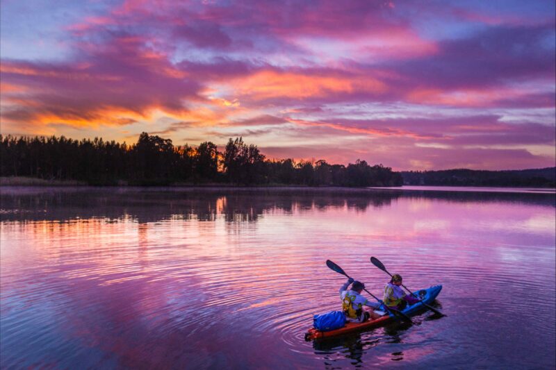 Two people in a kayak on a lake at dawn