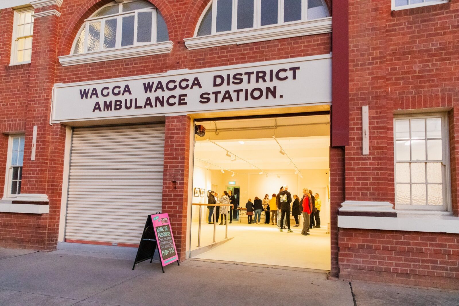 Photo of the front of old ambulance building, one roller door is raised to show event inside