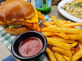Fish burger, tomato sauce and some chips sitting on a table
