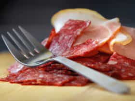 Sliced salami on wooden board with silver fork on top