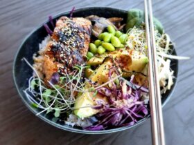 a bowl of delicious food including avocado, sprouts, salmon, rice, adamame beans with chop sticks