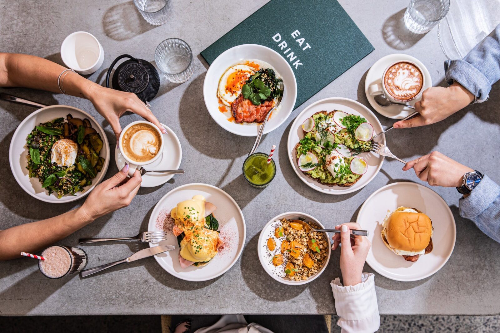 Flatlay photo of multiple dishes with three sets of hands eating the food