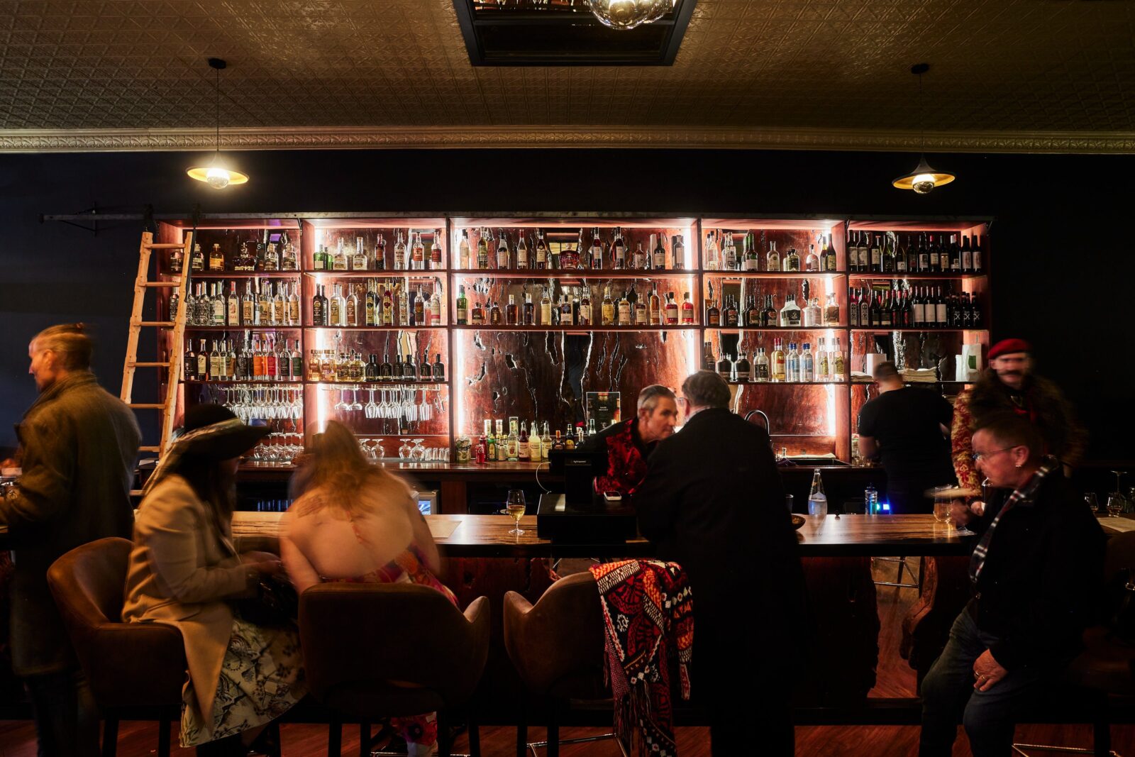 many people enjoying cocktails at a luxury bar featuring a library ladder and exotic spirits.