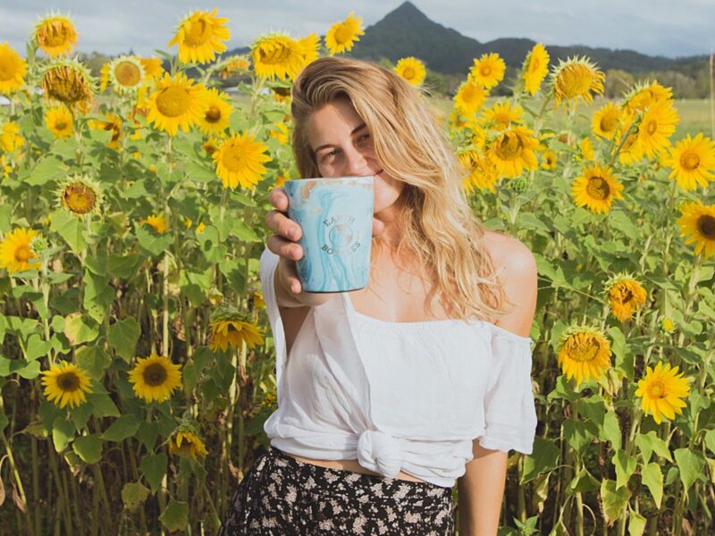 Lady holding mug up with sunflowers in background at the paddock project