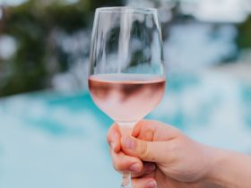 Hand holds out a chilled glass of rose with turquoise pool in background at The Terrace Bar