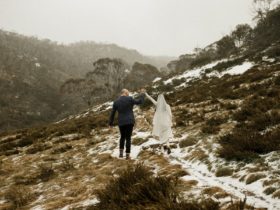 Bride and groom hold hands in the air walking through the snow
