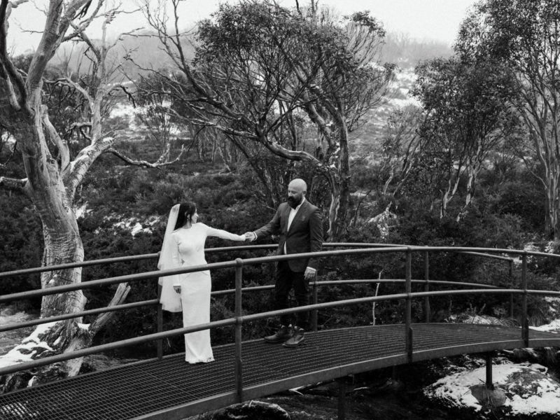 Bride and groom hold hands on a bridge with snow on the ground