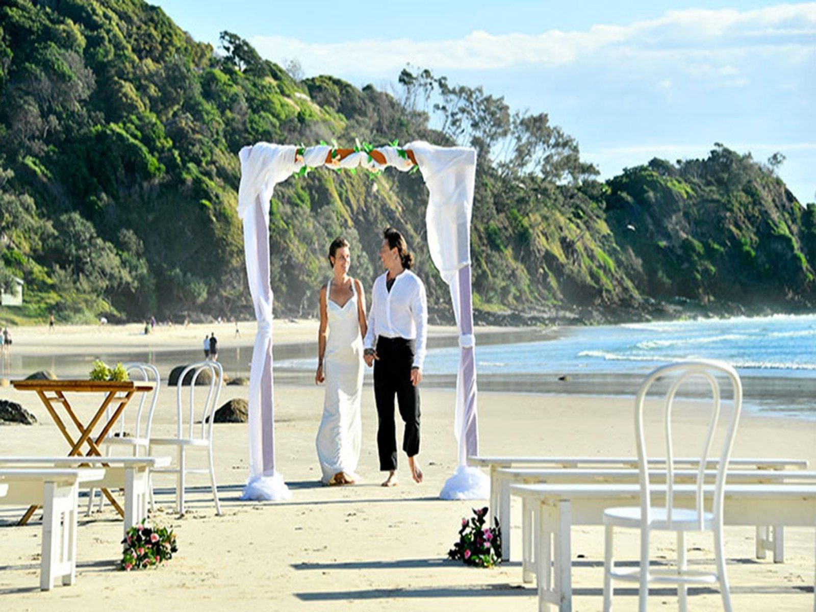 A couple under a wedding arch on Wategos Beach in Cape Byron State Conservation Area. Photo: Fiora