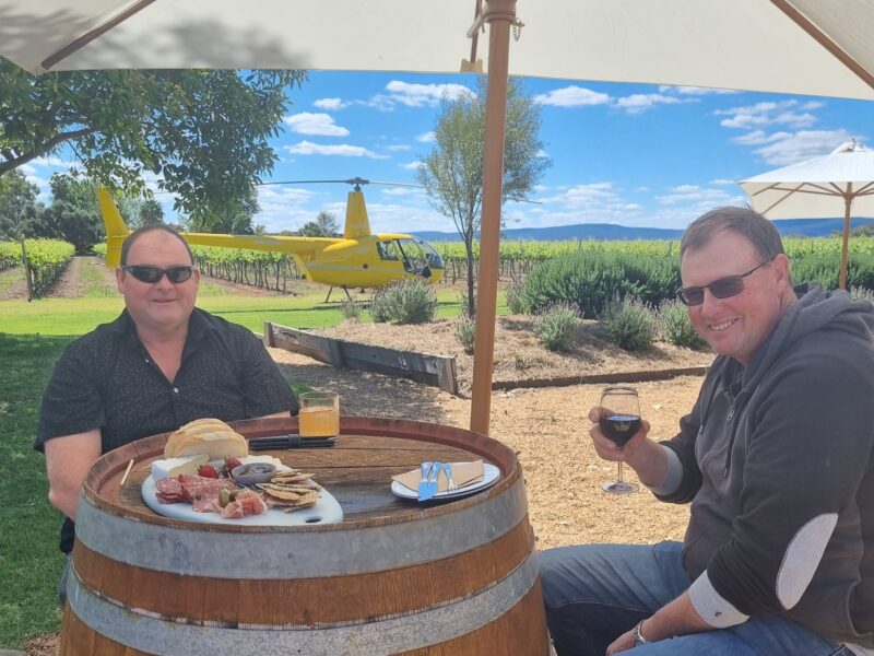 Two men enjoy a wine and cheese platter at Yarran Winery after arriving by Helicopter