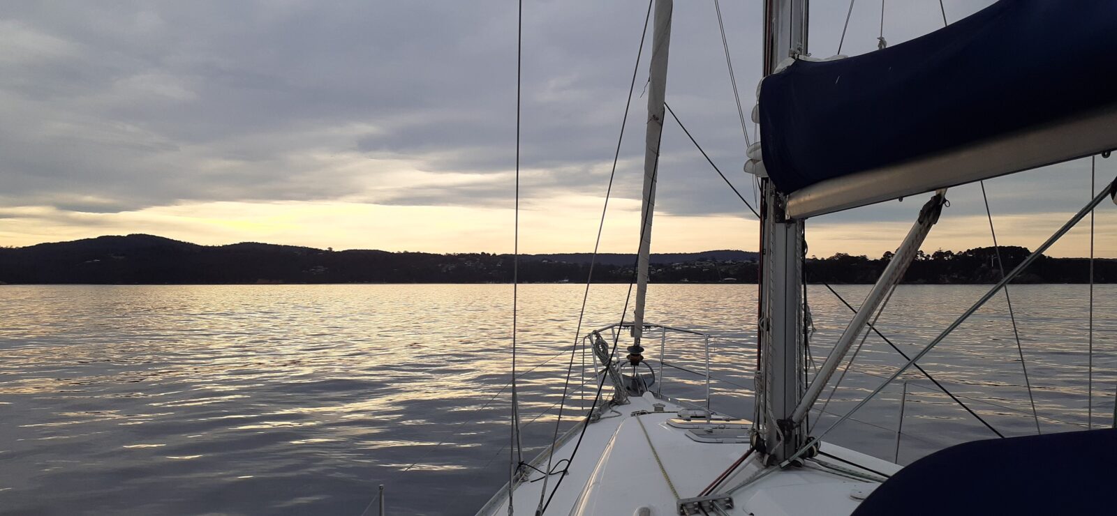 Luxury sailing boat sailing along smooth waters at sunset towards land