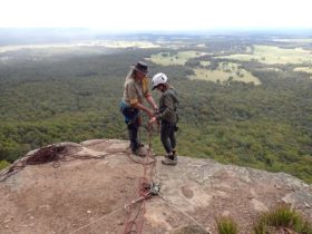 A guide and client are standing on top of a sixth meter abseiling cliff in Watagans National Park