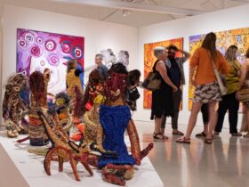 gallery with soft sculptures, aboriginal paintings in background and people looking at them