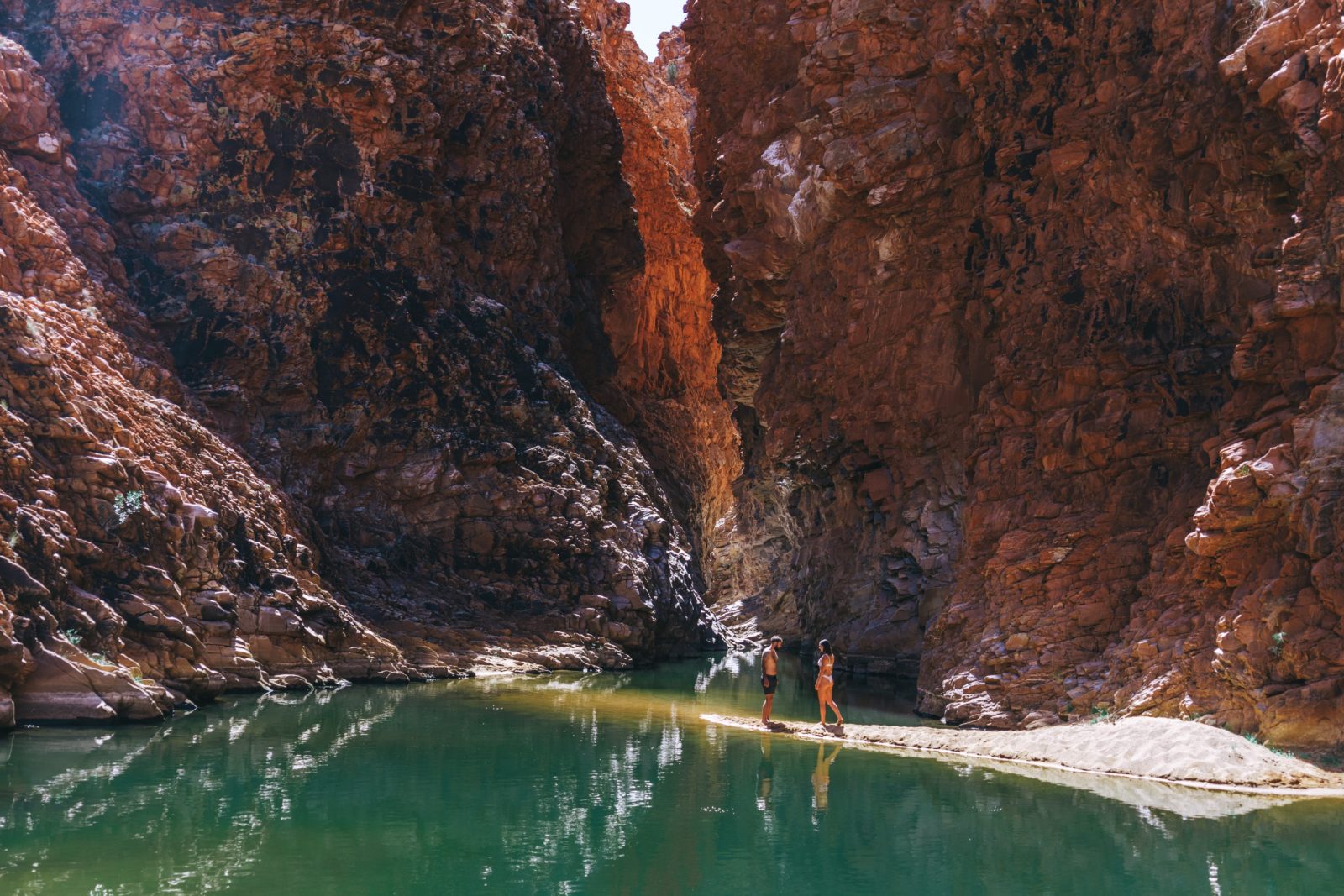 A couple walking on the banks of a waterhole at Redbank Gorge with the gorge in the background