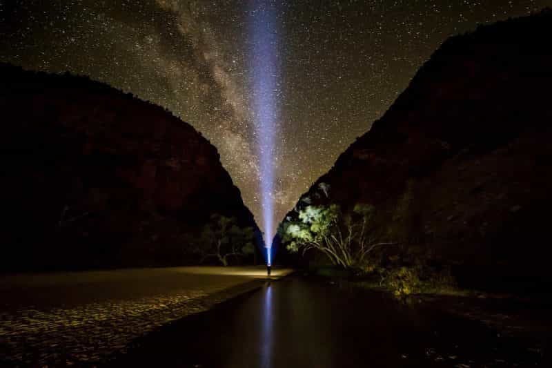 A traveller shines a torch towards the starry night sky with Simpsons Gap in the background