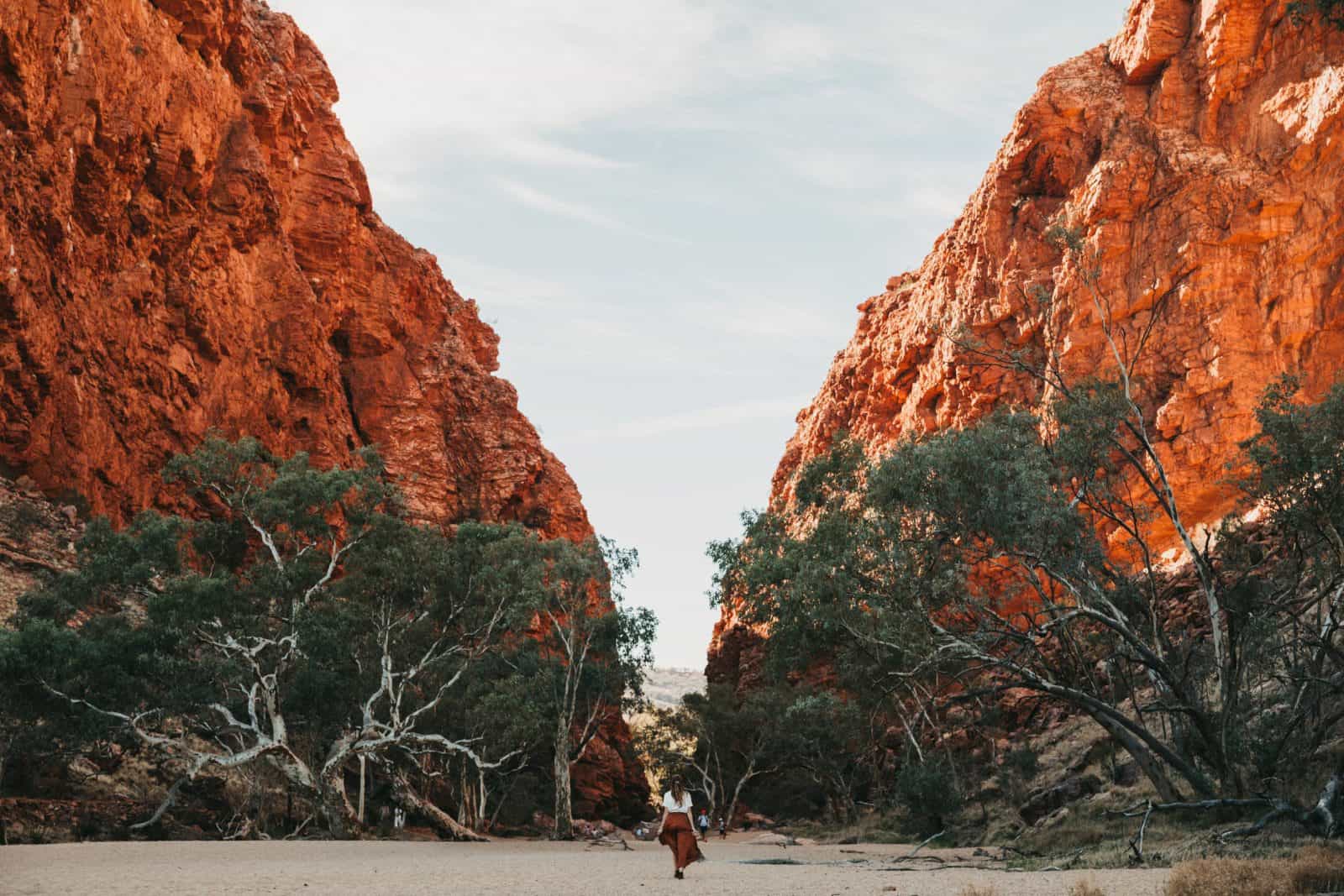 A woman walking in the dry river bed towards the enormous red escarpments of Simpsons Gap