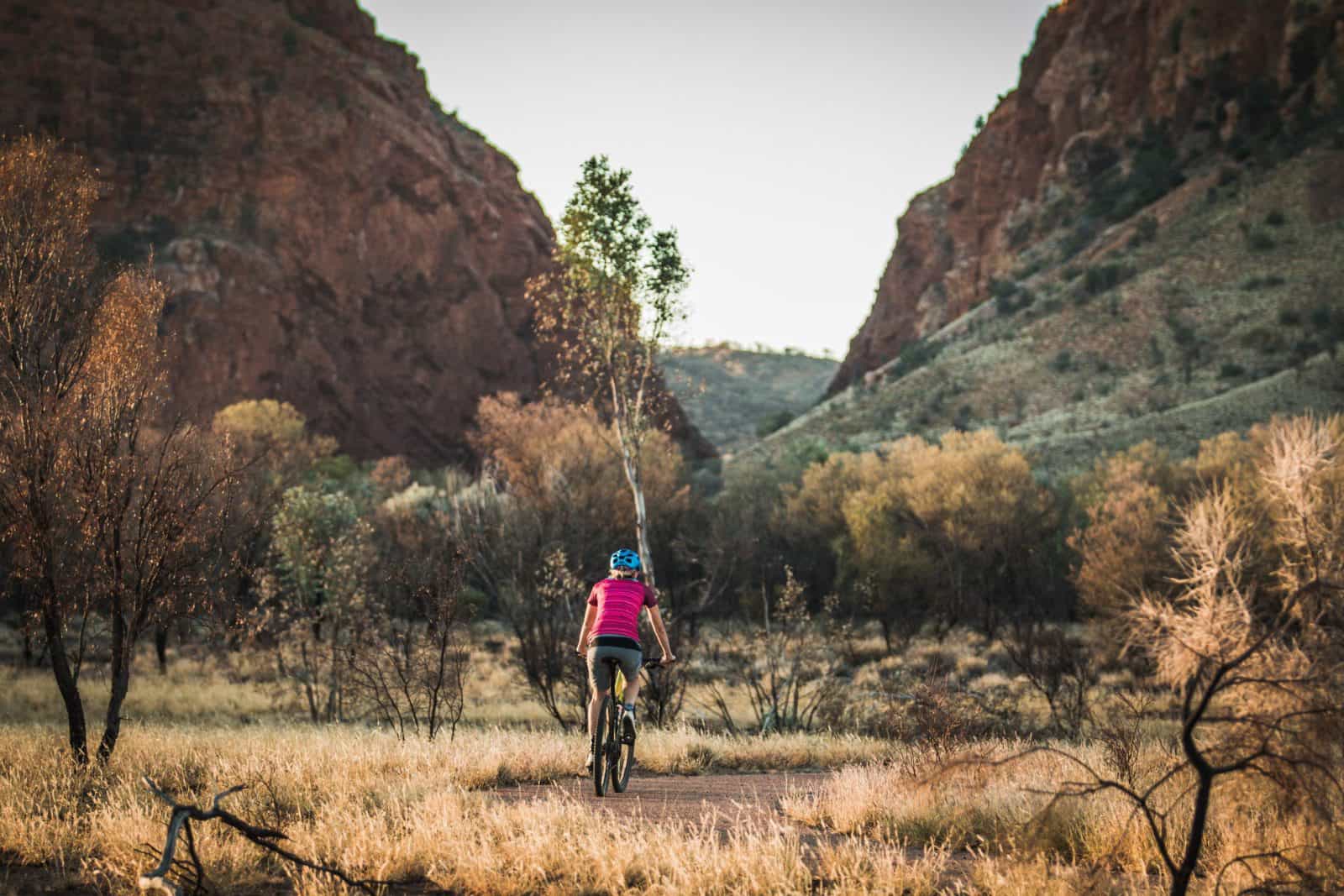 A woman rides a mountain bike on the bike path towards Simpsons Gap