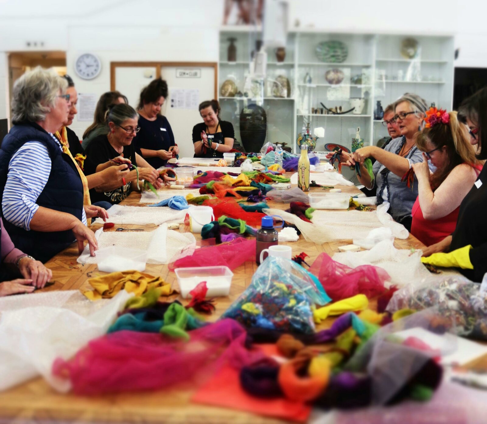 A group of women stand around a tall table with felting materials laid down in front of them