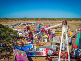Photo of show amusement rides against backdrop of rodeo arena and rural landscape