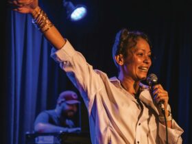 Photograph of artist Natalie with her hand in the air holding a microphone