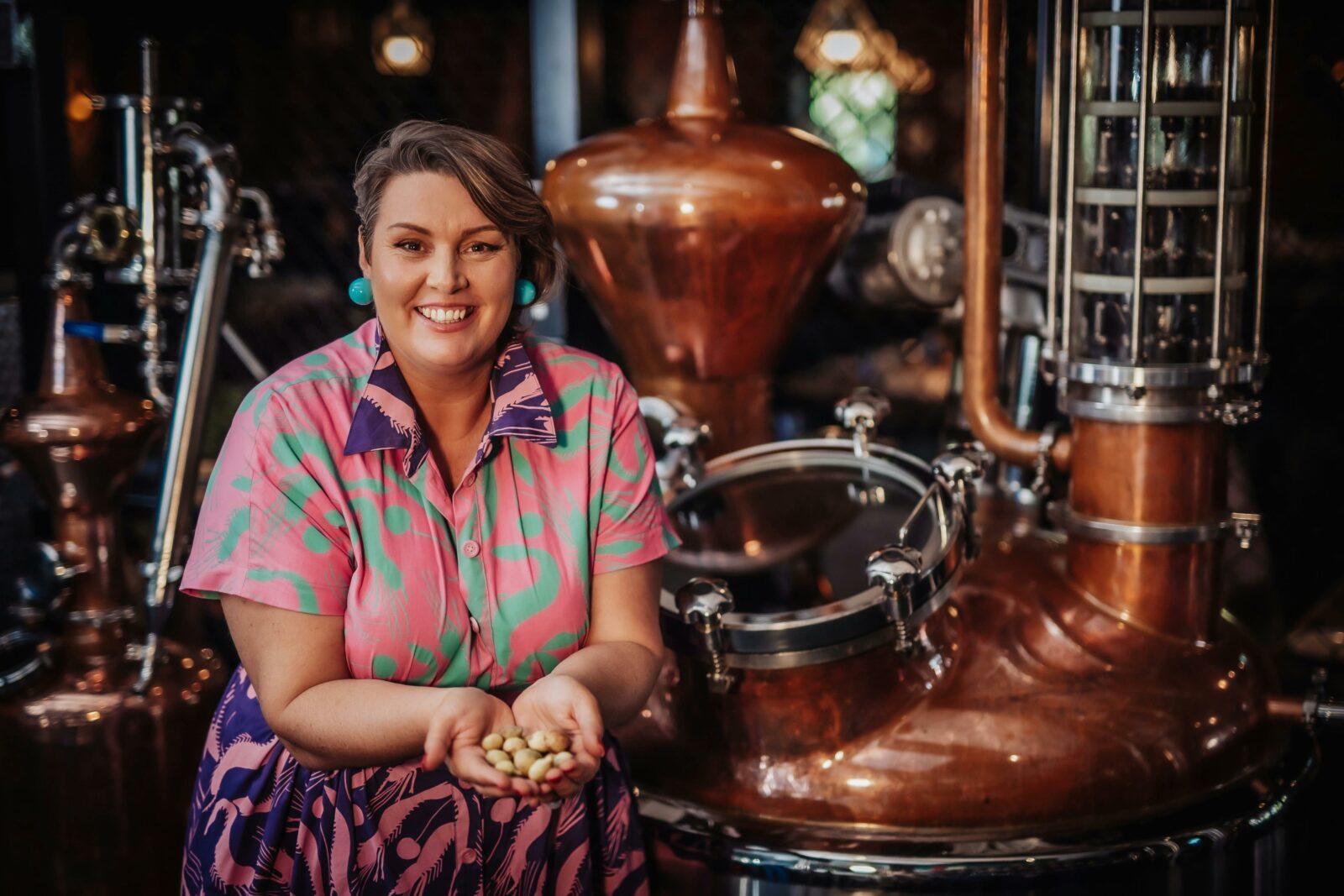 A woman standing in front of a copper distiller with native botanical fruit in her hands
