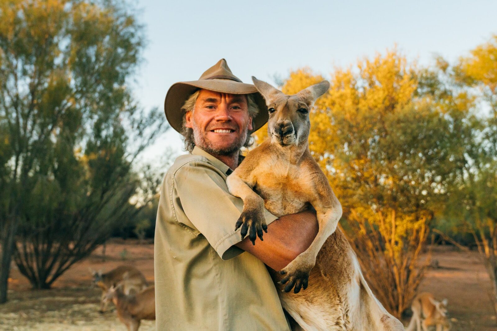 Chris Barns ('Brolga'), aka Kangaroo Dundee, cuddling a red kangaroo.