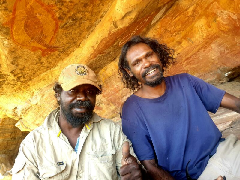 Two friendly aboriginal guides Sebastian and Gleeson with a back drop of ancient rock art