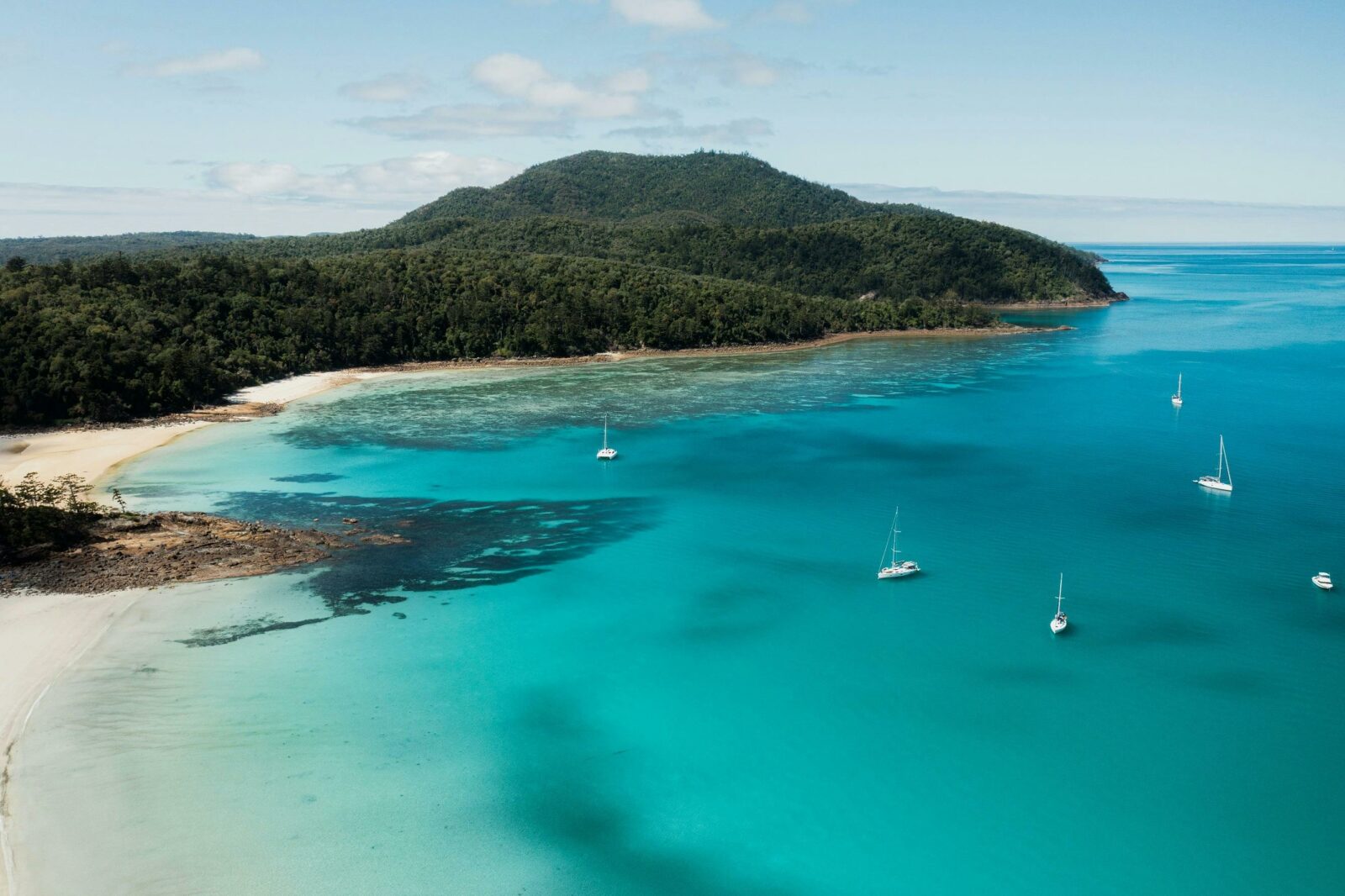 Aerial view of chance bay with sailing boats close to the beach and island hill covered in trees.