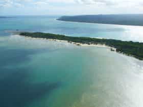 Aerial shot of the narrow tree-clad peninsula surrounded by sandy bays and turquoise waters.