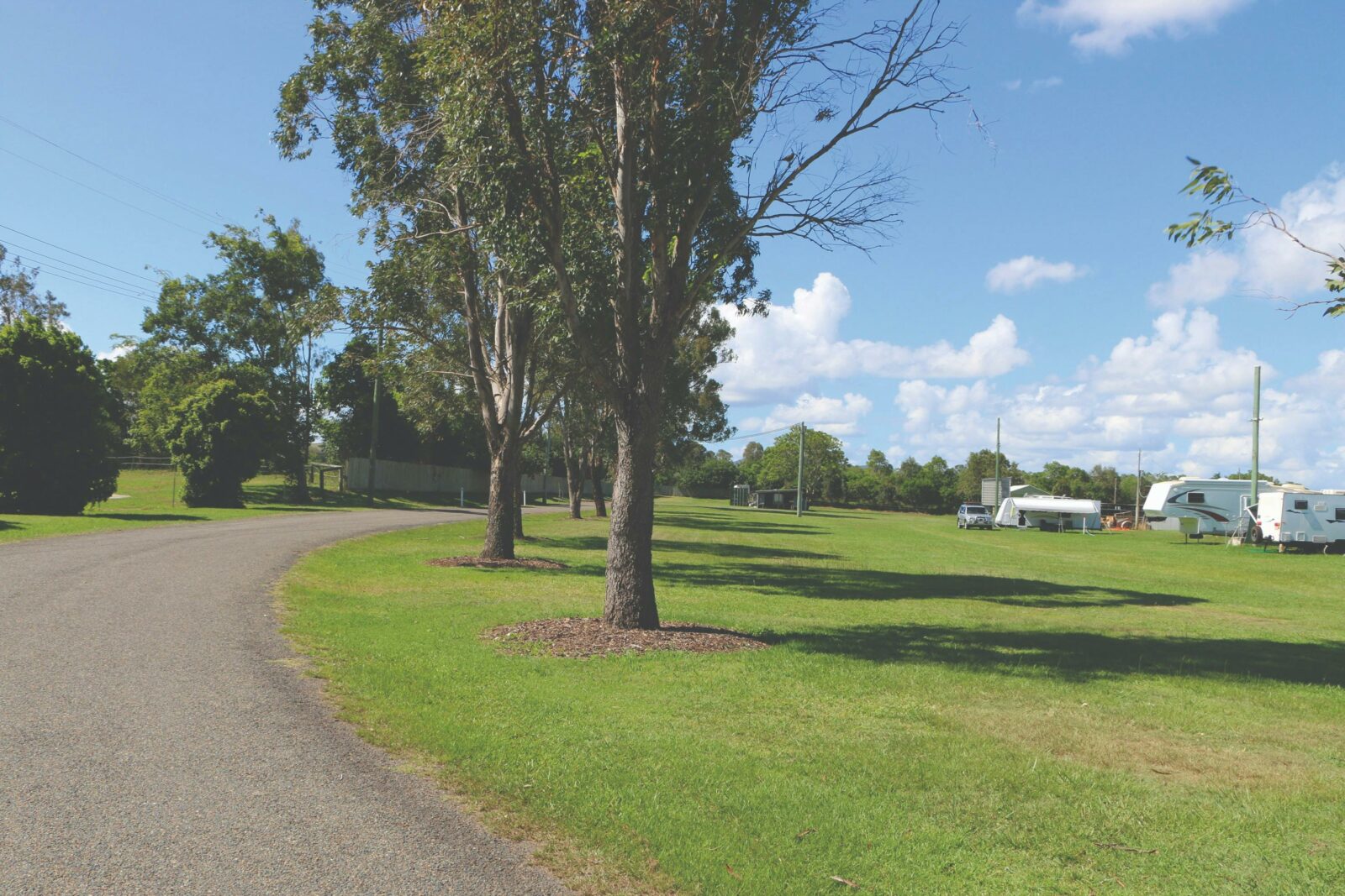 Kilcoy Showgrounds - part of the road with green grass, gumtrees and caravans in the distance.