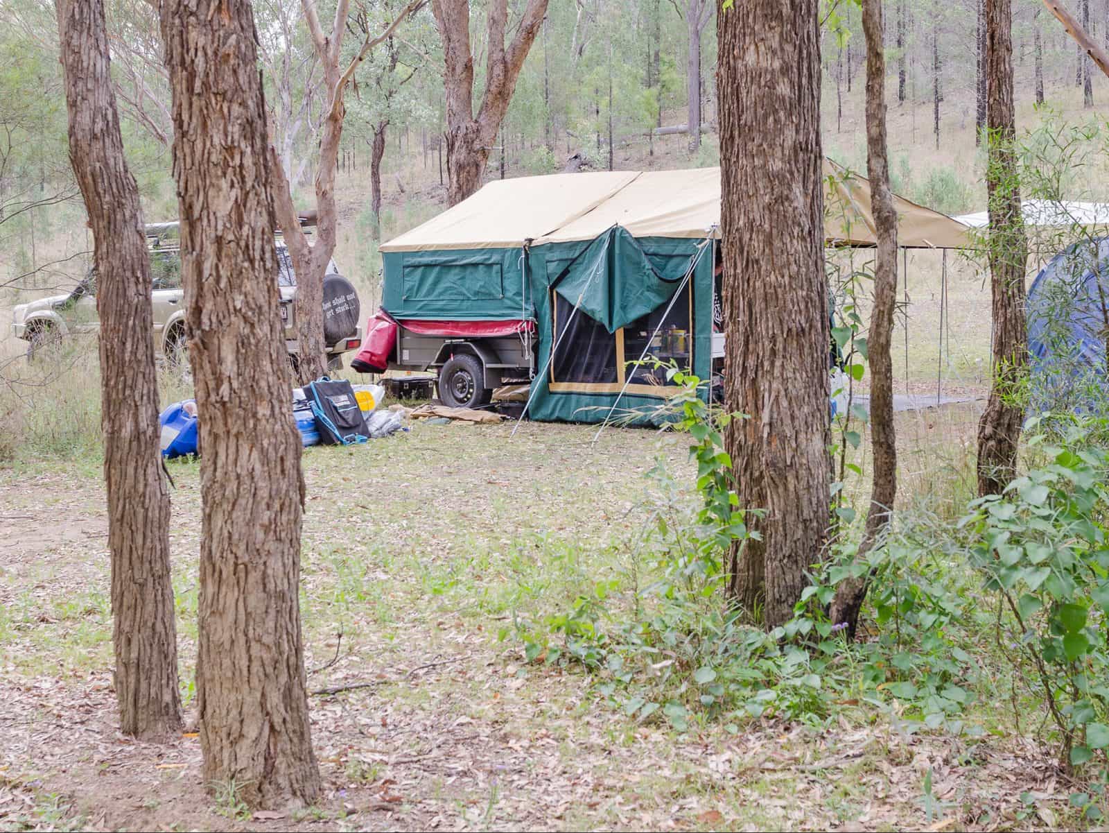 Camper trailer and 4WD set up under trees.