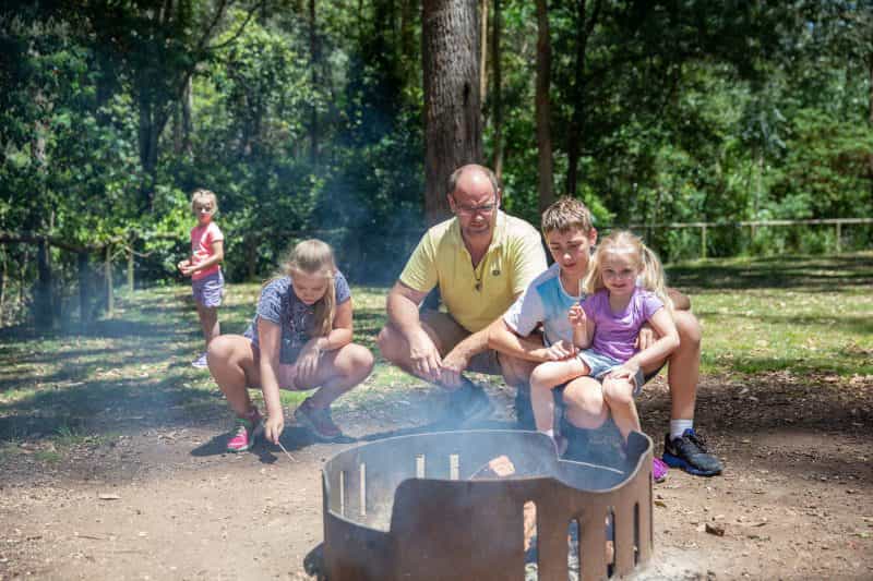 Dad and three kids kneeling beside a fire pit trying to make a fire