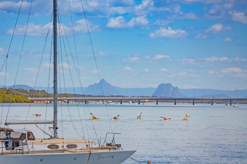 A number of people Kayaking with views of the Bribie Island Bridge and Glasshouse Mountains