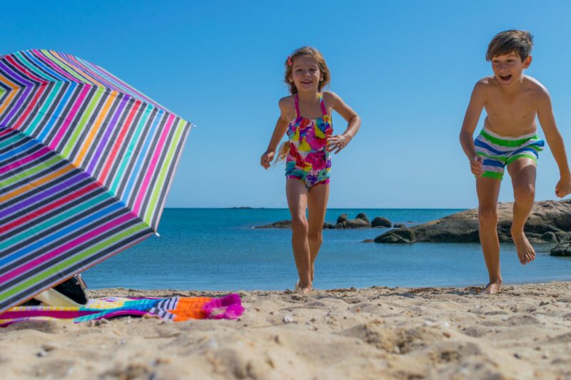 Children playing at sandy beach on sunny day, beach umbrella and beach toys