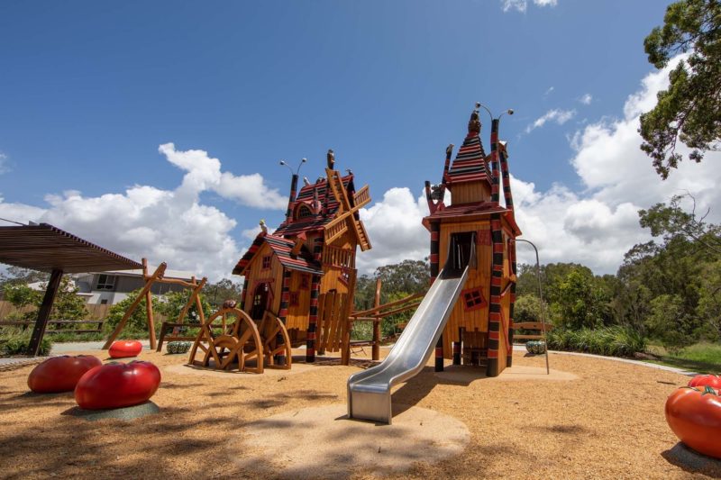 Two Halloween themed playground towers with a metal slide and a swing set on a gravel ground