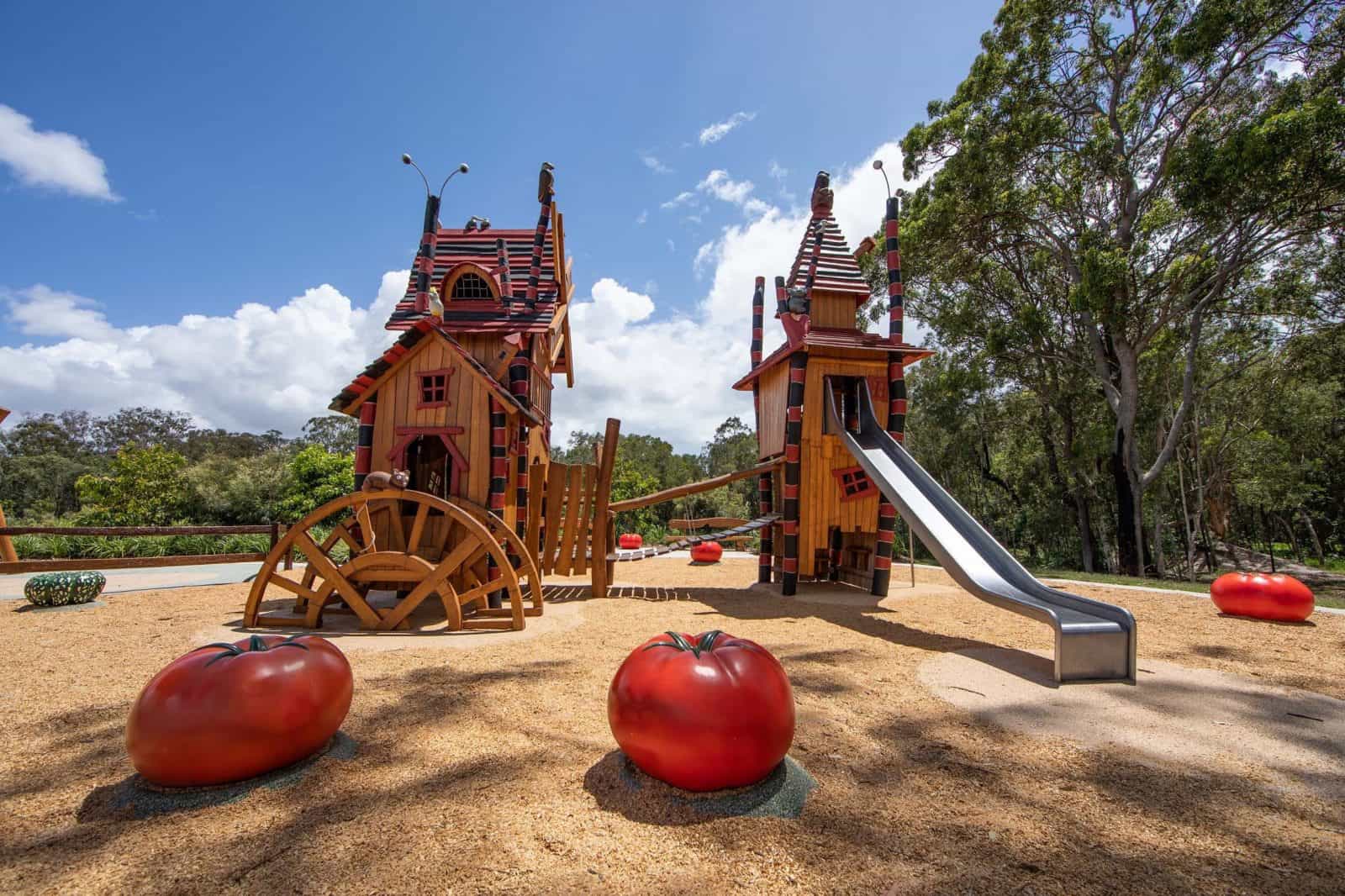 Two Halloween themed playground towers with a metal slide and two over sized tomatoes in foreground