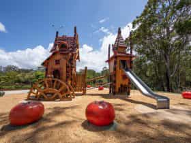 Two Halloween themed playground towers with a metal slide and two over sized tomatoes in foreground
