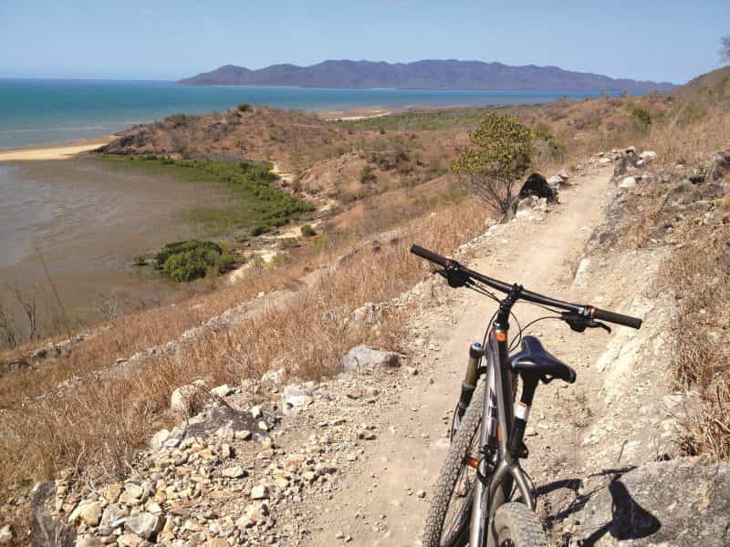 Mountain bike parked on dirt trail winding around a hill slope with a view over headland, ocean