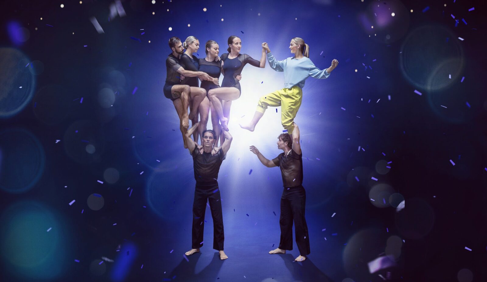 Performers standing on top of each other surrounded by a blue sparkly background.