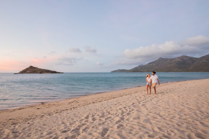 A happy couple walking along the sandy beach during sunset, hilly islands in the background