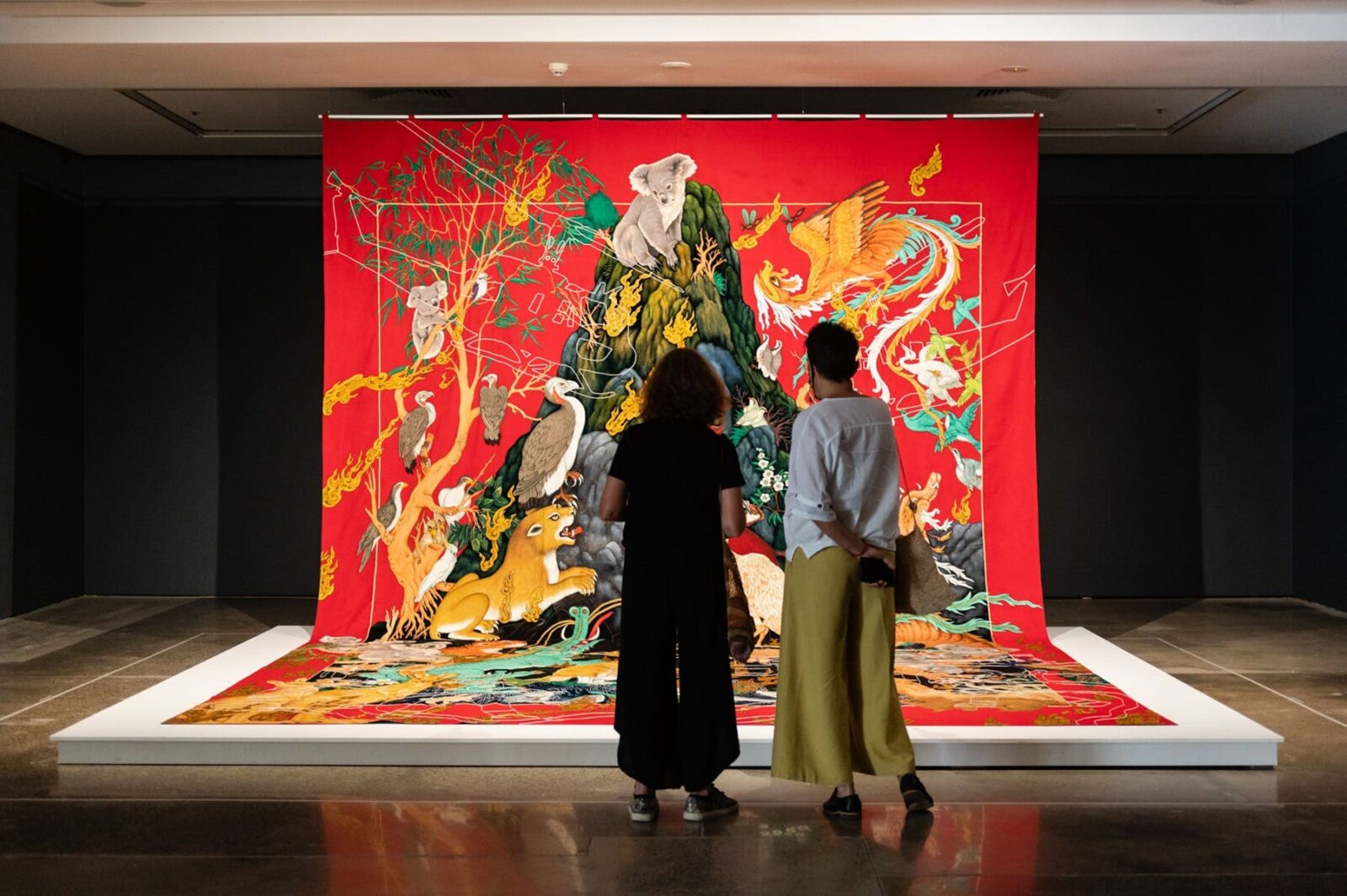Two women from behind looking at a very large tapestry with Australian animals