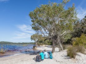 photo showing two hikers sitting on a sandy beach at Lake Birrabeen