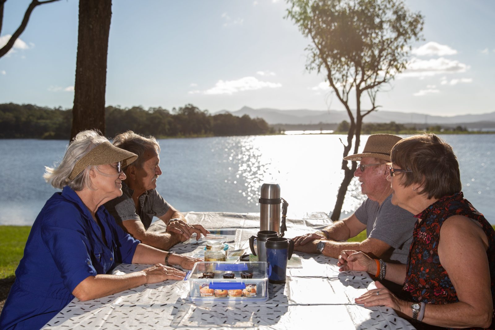 Two elderly couples sitting at a picnic table beside Lake Samsonvale eating and drinking tea