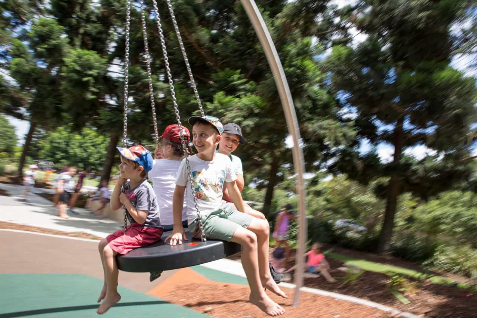 Four kids sitting on a large round swing at Pine Rivers Park