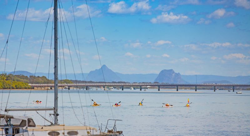Five kayaks in the shallow waters heading away from Bribie Island bridge